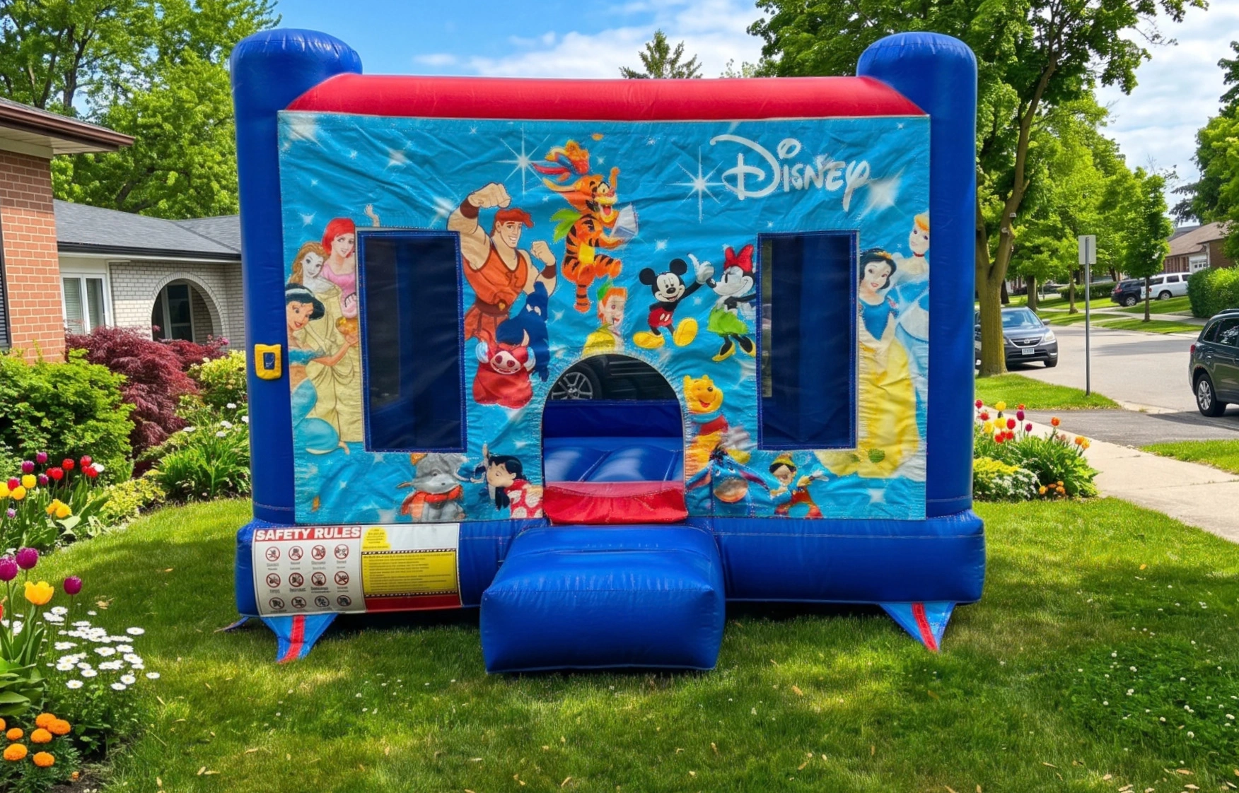 Small Disney K3 bouncy castle with blue towers, red trim and Disney character artwork on a front lawn — The Bouncy Castle King, serving Brampton and the GTA