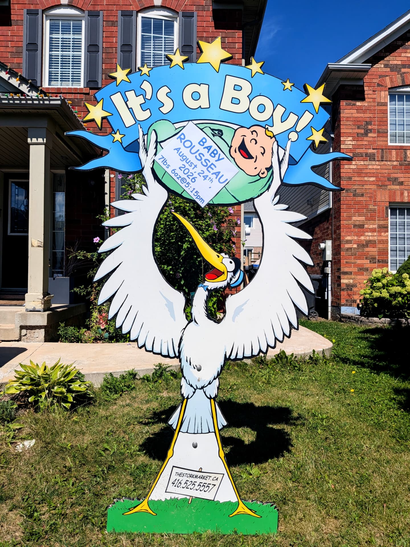 Blue lawn stork birth announcement sign for Baby Rousseau in front of a red brick home — The Stork Market, serving Brampton and the GTA
