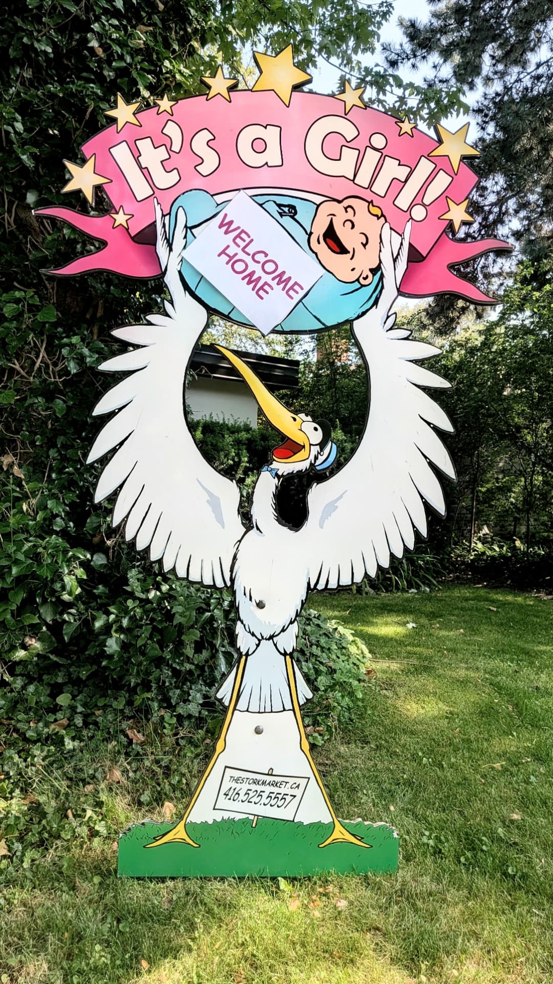 Pink Welcome Home lawn stork sign in front of green foliage — The Stork Market, serving Brampton and the GTA