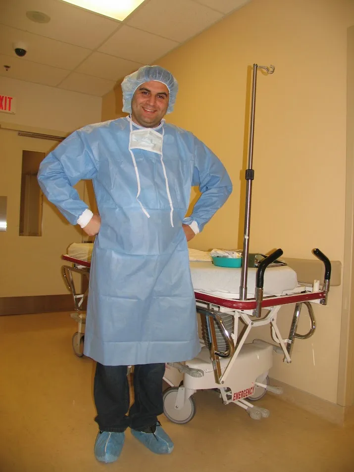 Smiling new dad in a blue hospital gown, cap and shoe covers ready for the birth of his baby girl